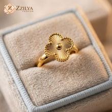 Golden clover ring with sunburst design on a soft fabric surface, branded 'ZZILYA'.