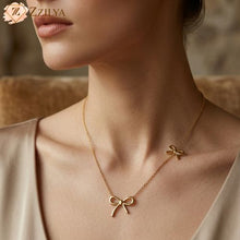 Close-up of a woman wearing a Zzilya Fashion golden anti-tarnish necklace featuring two delicate bow pendants—one centered and one smaller bow positioned off-center along the chain; styled with a champagne silk top.