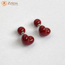 Red heart-shaped earrings on a white background with 'ZZILYA' branding.