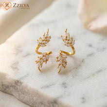 Elegant gold-plated ear cuffs featuring a dual leaf design studded with marquise-cut white stones on a marble surface by Zzilya Fashion.