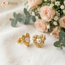 Gold heart-shaped earrings with pearls on a white fabric background with flowers by Zzilya Fashion