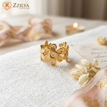 A wide golden anti-tarnish ring with a textured daisy floral pattern, resting on white textured fabric next to dried white flowers and a soft-lit candle in the background by zzilya Fashion
