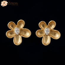 Gold flower-shaped earrings with a central gemstone on a black background, branded 'ZZILYA'.