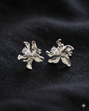 Pair of silver organic-shaped flower stud earrings with a teardrop crystal center, displayed on a black textured fabric background.