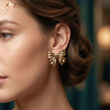 Gold bow-shaped earring worn by a model with a blurred background by Zzilya Fashion