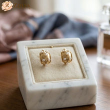 Gold earrings with pearl details on a marble stand, brand 'zzilya' visible.