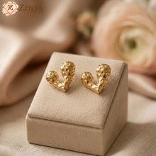 18k plated Gold heart-shaped earrings on a beige jewelry box with a blurred floral background by Zzilya fashion