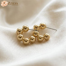 Gold hoop earrings on a beige fabric background with 'Zzilya Fashion' branding.