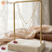 Gold necklace with a butterfly pendant on a decorative stand, branded 'ZZILYA'.