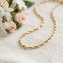 Gold twisted necklace on a textured surface with flowers in the background, featuring the zzilya fashion brand.