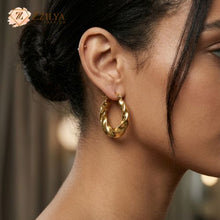 side profile of a woman wearing a thick, golden twisted hoop earring from ZZILYA Fashion. The earring features a 
