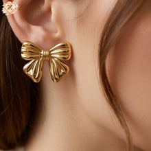 Gold bow-shaped earring worn by a person with a blurred background by Zzilya fashion