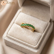 Gold ring with green gemstones on a beige jewelry box, branded 'ZZILYA'.