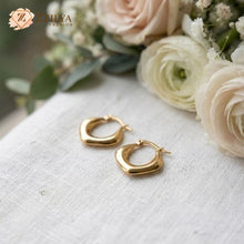 Gold hoop earrings on a white fabric surface with flowers in the background by Zzilya Fashion Jewellery