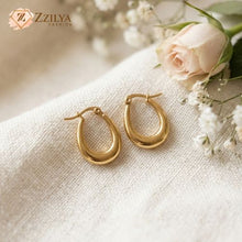 Gold hoop earrings on a textured surface with flowers, featuring the brand 'ZZILYA'.