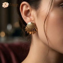 Close-up of a woman wearing a large, polished gold seashell statement earring by ZZILYA Fashion. The earring features a detailed scallop design with a high-shine metallic finish, styled to elevate a sophisticated vacation outfit.