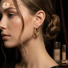 Close-up of a woman wearing gold hoop earrings with a blurred background by Zzilya Fashion