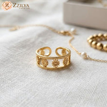 Gold sunburst ring with floral designs on a light fabric background, branded 'Zzilya Fashion'.