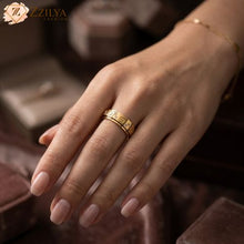 Golden cartier double band ring on a hand with a blurred background, featuring the brand 'ZZILYA'.