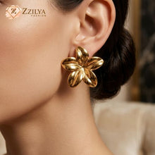 A woman with a sleek bun wearing a bold, five-petal golden floral earring with a high-shine finish from Zzilya Fashion.