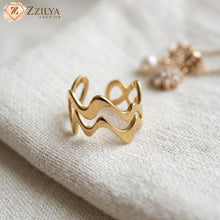 Minimalist golden zig zag anti-tarnish ring by Zzilya Fashion displayed on a cream textured fabric background with a soft-focus jewelry detail in the rear.
