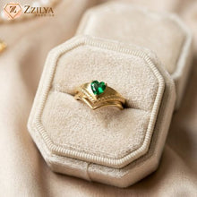 Gold ring with a green gemstone on a beige jewelry box, branded 'Zzilya'.