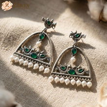Ornate silver earrings with green stones and pearls on a textured fabric background by zzilya fashion