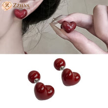 Heart-shaped red earrings being worn and displayed on a plain background with Zzilya Fashion logo.