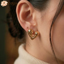 Close-up of a person wearing gold heart-shaped earrings with a blurred background by Zzilya fashion