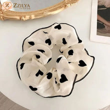 White scrunchie with black heart patterns on a white surface, branded 'Zzilya'.