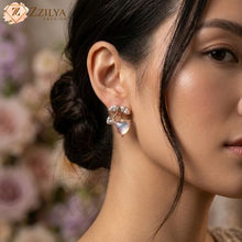 Close-up of a woman wearing a Golden earring with a blurred floral background, featuring the brand 'ZZILYA'.
