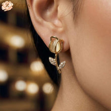 Close-up of a gold tulip-shaped earring worn by a person with a blurred background by zzilya fashion
