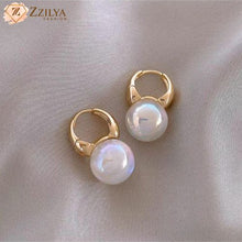 Gold hoop earrings with pearls on a light fabric background, branded 'Zzilya'.
