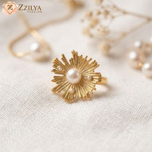 Large golden anti-tarnish statement ring with a textured sunburst floral design and a large central pearl, worn on a model's hand to showcase its bold, sculptural 2026 jewelry trend style. by zzilya fashion jewellery
