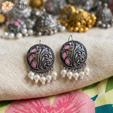 Ornate earrings with pink centers and pearl drops on a textured fabric background, featuring the brand 'Zzilya'.