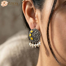 Close-up of an oxidized earring with yellow stones and pearl hangings intricate design worn by a women, branded 'Zzilya'.