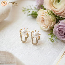 Pearl earrings with gold accents on a white surface with flowers in the background, featuring the brand 'Zzilya'.