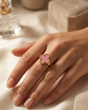 Hand wearing a pink clover-shaped ring on a light surface with a blurred background by Zzilya fashion Jewellery
