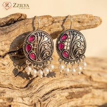 Decorative earrings with pink stones and pearl-like beads on a wooden surface, branded 'ZZILYA'.