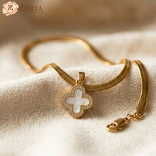 Gold necklace with a clover-shaped pendant on a soft beige background, featuring the brand 'Zzilya'.