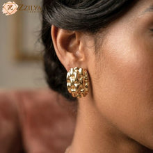 Close-up of a person wearing gold earrings with 'Zzilya' branding.