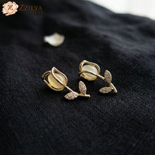 Gold floral earrings with gemstones on a dark fabric background, featuring the brand 'ZZILYA'.