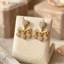 Gold heart-shaped earrings on a display card with 'Zzilya' branding.