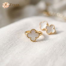 Gold Clover ring with white enamel on a soft fabric background, featuring the brand 'ZZILYA'.
