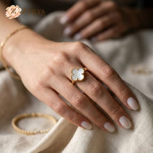 Close-up of a hand wearing a gold Clover ring with a white enamel on a neutral background by zzilya fashion