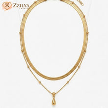 ZZILYA Fashion double-layered gold neckchain featuring a flat herringbone chain and a beaded chain with a polished teardrop pendant on a white fabric background.