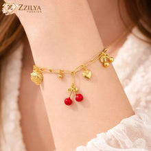Close-up of a gold charm bracelet on wrist, featuring red cherry and gold fruit motifs anti tarnish by zzilya fashion jewellery