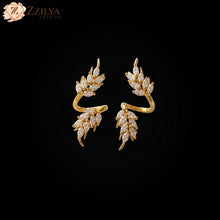 Elegant gold-plated ear cuffs featuring a dual leaf design studded with marquise-cut white stones on a marble surface by Zzilya Fashion.