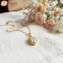 Gold necklace with a heart-shaped pendant on a white fabric background with flowers by zzilya fashion