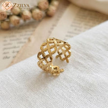 A gold-plated anti-tarnish ring with a floral cut-out pattern, resting on a white textured cloth with dried roses and a book in the blurred background by zzilya fashion 